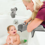 Happy baby in a white tub, smiling as a woman uses a gray Skip Hop Moby rinser to pour water.