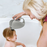 Mom rinses baby's hair with a gray Skip Hop Moby Waterfall Rinser, shaped like a whale, in a white bathtub.