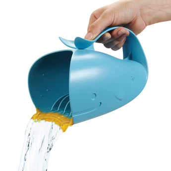 Hand holding a blue whale-shaped Skip Hop Moby Waterfall Rinser pouring water, with a soft yellow rubber lip.