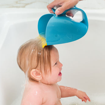Blue whale-shaped Skip Hop Moby Waterfall Rinser pouring water over a baby's head in a white tub.