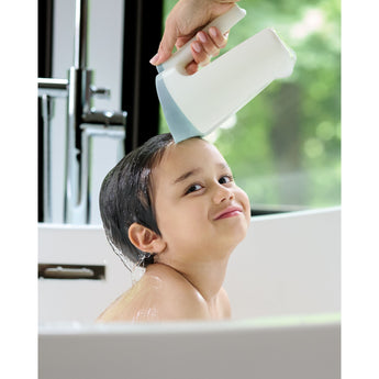 Hand holding a white and blue Skip Hop Moby Waterfall Rinser over a smiling child's head in a white tub.