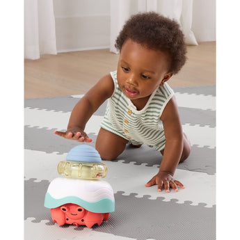 Baby on a gray and white mat reaching for a colorful Skip Hop Stack & Crawl 4-in-1 Crab toy.