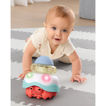 Smiling baby crawling towards a Skip Hop Stack & Crawl 4-in-1 Crab toy with glowing lights.