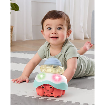 Smiling baby on a gray and white mat playing with a colorful Skip Hop Stack & Crawl 4-in-1 Crab toy.