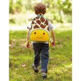 Toddler boy wearing a Skip Hop Zoo Giraffe Backpack with brown spots and yellow face, walking in grass.