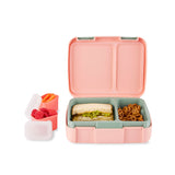 Open pink and teal Skip Hop Zoo bento box with sandwich and pretzels, plus two small containers of fruit and carrots.