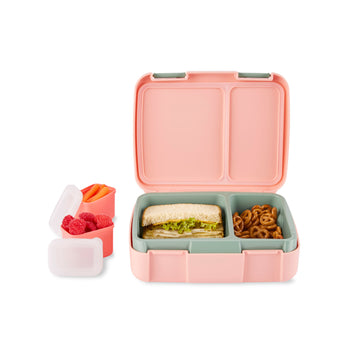 Open pink and teal Skip Hop Zoo bento box with sandwich and pretzels, plus two small containers of fruit and carrots.