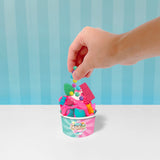 Hand adding colorful beads to a pink slime "gelato" in a branded cup with blue and pink accents.