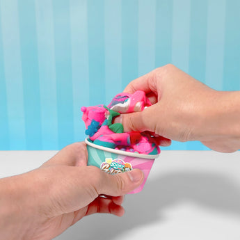 Hands holding a colorful Slimy Gelateria cup filled with pink, blue, and white slime, decorated with a cherry.