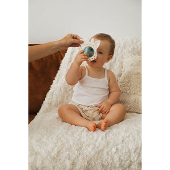Baby in white tank top and patterned diaper holding a Sophie la girafe Magic Mirror SIGHT White teething toy.