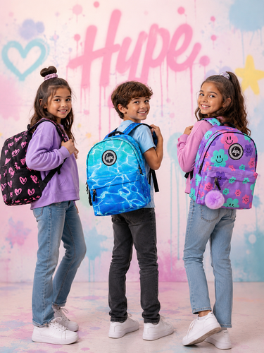 Three children standing in a studio wearing colorful Hype backpacks, with a pink and blue Hype-branded backdrop behind them.