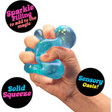 Hand squeezing a blue, glitter-filled NEE DOH Dream Drop squishy fidget toy.