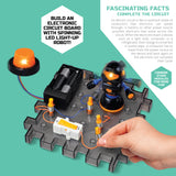 Child's hand building a Discovery Mindblown circuit board with a black and orange LED robot spinner and orange light.