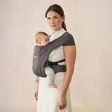 Woman wearing a heather grey Ergobaby Embrace newborn carrier with a baby facing inward.