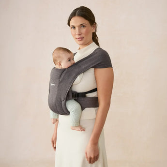 Woman wearing a heather grey Ergobaby Embrace newborn carrier with a baby facing inward.