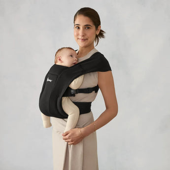 Woman wearing a black Ergobaby Embrace newborn carrier with a baby facing inward.