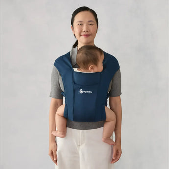 Woman wearing a navy Ergobaby Embrace carrier with a baby sleeping against her chest.