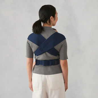 Woman from behind wearing a heather grey Ergobaby Embrace carrier with navy blue straps.