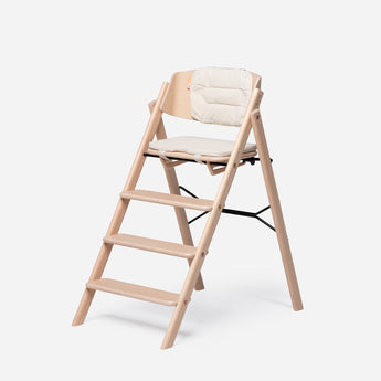 Light wood highchair with a cream, padded, reversible cushion set on the seat and backrest.