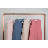 Four Lulujo 100% cotton muslin sleep sacks in pink, blue, beige, and coral, hanging on a copper rail.
