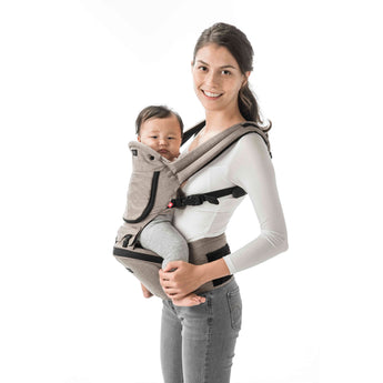 Smiling mom carrying baby in a light brown MiaMily Hipster ergonomic baby carrier with hip seat.