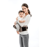 Smiling mom holds baby in a beige MiaMily Hipster ergonomic baby carrier with a black hip seat.