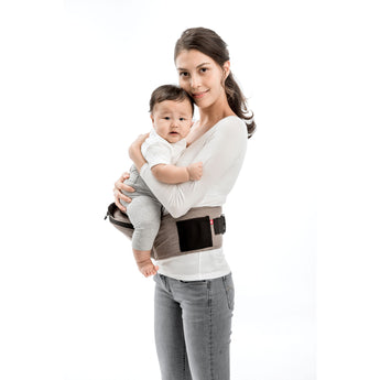 Smiling mom holds baby in a beige MiaMily Hipster ergonomic baby carrier with a black hip seat.