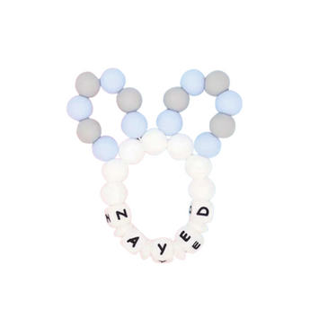 Personalized blue, grey, and white silicone bunny ears teether with "ZAYED" spelled in black letters.