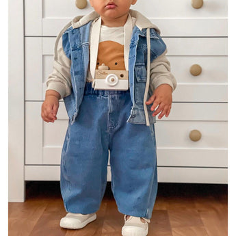 Baby wearing a personalized white wooden camera toy with a strap, denim outfit, and neutral top.
