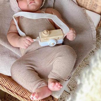Baby in neutral knit outfit holding a personalized wooden camera toy with white lens and strap.