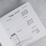 Open white baby milestone album page with Arabic text, dotted lines, and small eye illustrations.