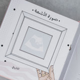 Open pink suede baby milestone album page with "صورة الأشعة" (ultrasound photo) title and framed ultrasound illustration.