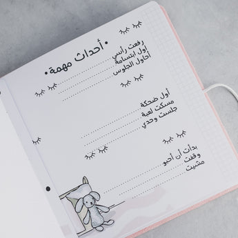 Open baby milestone photo album page with Arabic text, "أحداث مهمة," and a cute bunny illustration.