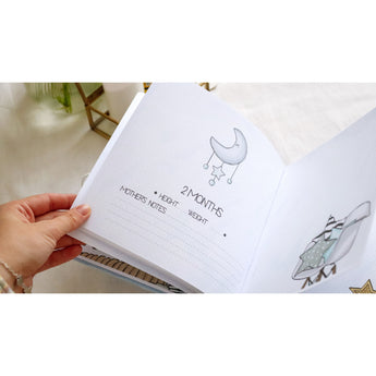 Hand turning a page of a personalized baby milestones photo album with a moon and stars illustration.