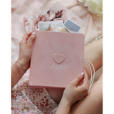 Hands holding a pink suede baby milestones photo album with an embossed heart and "GIRL" text.