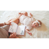 Baby on a cream blanket, looking at a person holding an open pink personalized baby milestones photo album.