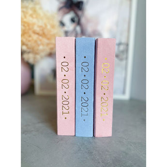 Three personalized suede baby milestone photo albums: two pink, one blue, with gold foil dates.