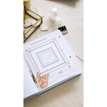 Open baby milestone photo album showing an "Ultrasound Scan" page with a framed illustration of a baby.