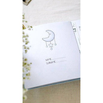 Open baby milestone photo album page with a moon and stars illustration, dotted lines for name/surname.