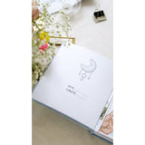 Open baby blue personalized milestone photo album with a moon and stars design, showing name/surname lines.