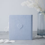 Light blue suede baby milestones photo album with an embossed heart, white ribbon, and a blue glass vase.