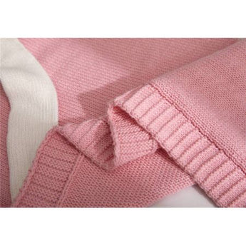 Close-up of a soft, pink knit blanket with a white stripe, showing ribbed edges and cozy texture.