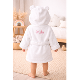 White organic cotton baby hooded bathrobe with bear ears and "Mila" embroidered in pink on the back.