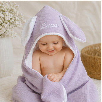 Smiling baby in a personalized lavender organic cotton bunny hooded towel with white trim and "Luna" embroidery.