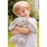 Blonde child hugging a soft gray personalized bunny plush toy with "Mark" embroidered on its ear.
