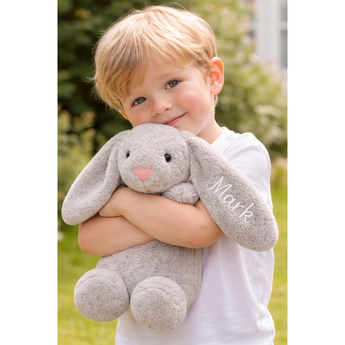 Blonde child hugging a soft gray personalized bunny plush toy with "Mark" embroidered on its ear.
