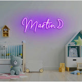 Purple LED neon sign "Martin D" in script font, mounted on a white wall above a crib.