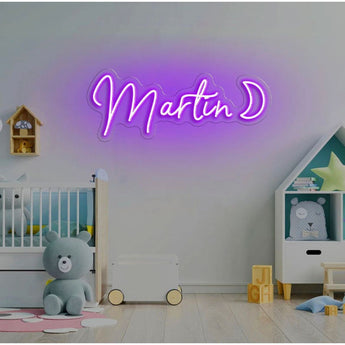 Purple LED neon sign "Martin D" in script font, mounted on a white wall above a crib.