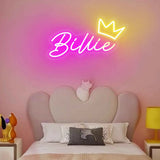 Pink neon "Billie" sign with a yellow crown, above a bed with a heart-shaped headboard.