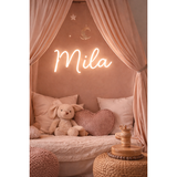 Pink personalized LED neon sign "Mila" in a cozy bedroom nook with a plush bunny and heart pillow.
